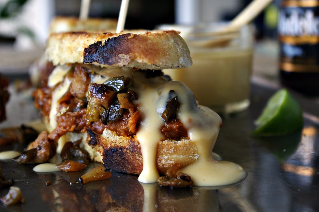 Chipotle Lime Brisket Sandwich topped with Sauteed Brussels Sprouts, Onions and Peppers AND Modelo Cheese Sauce